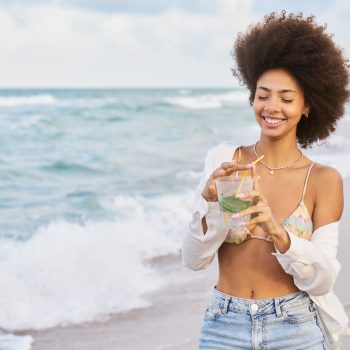 A woman is smiling and holding a drink in a glass
